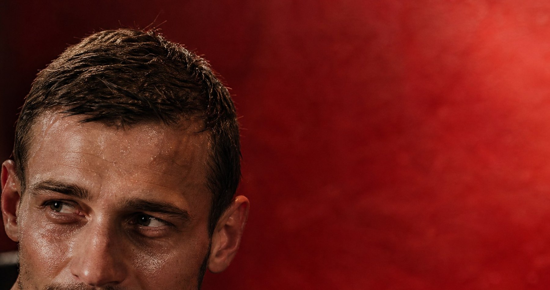 Close portrait, half in shadow, against a deep red wall